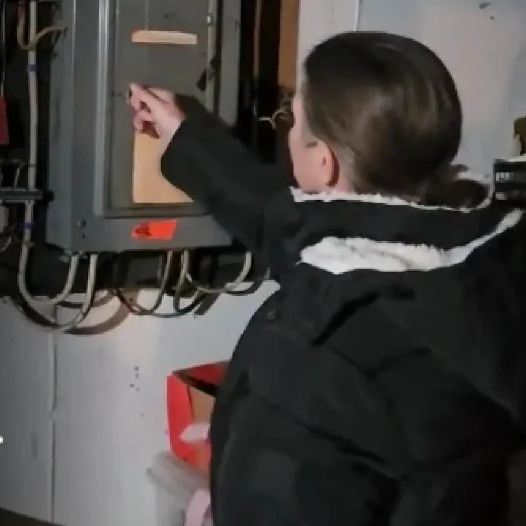 Person inspecting an electrical panel in a dimly lit room.